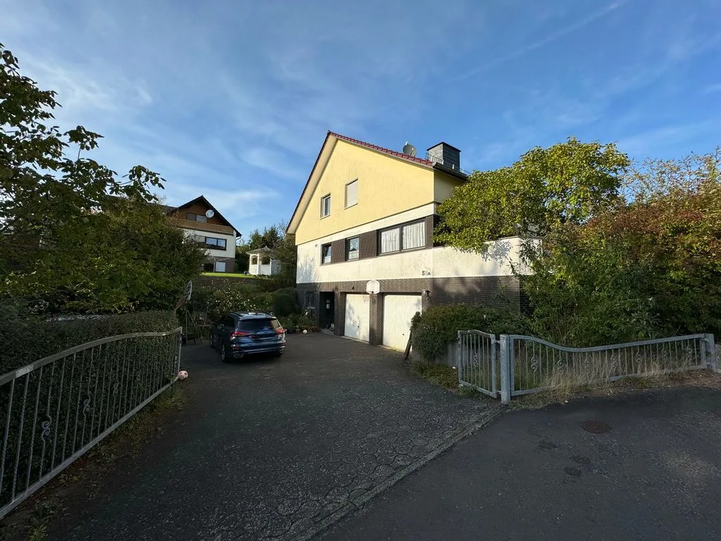 Wohnhaus mit gelber Fassade und Garagen von vorne, Zufahrt mit parkendem Pkw, bei Tageslicht.