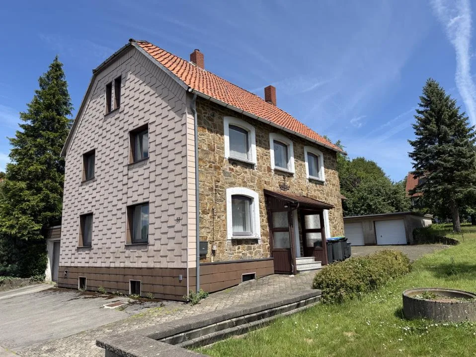 Außenansicht des Wohnhauses mit Natursteinfassade, Satteldach und Garage im Hintergrund.