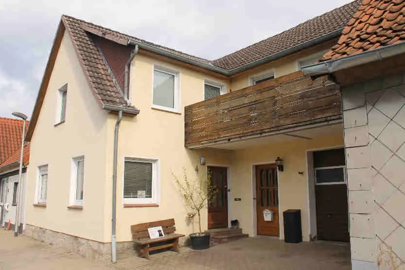 Außenansicht des Wohnhauses mit Holzbalkon und Hauseingang, Frontalaufnahme