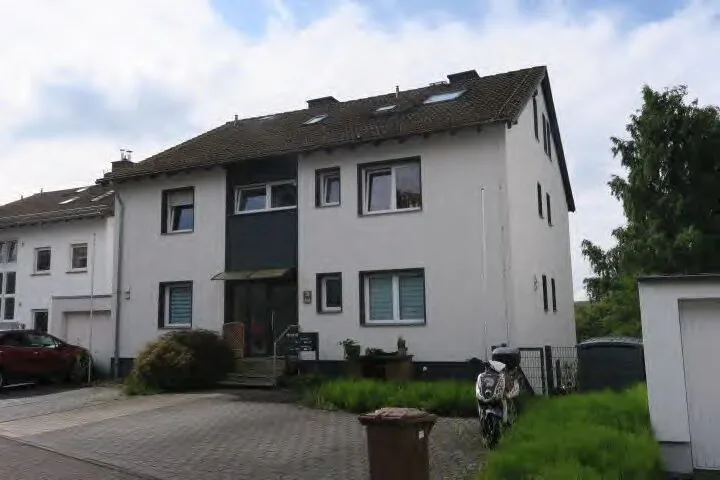 Außenansicht eines weiß verputzten Mehrfamilienhauses mit Satteldach, Vorgarten und Zufahrt.