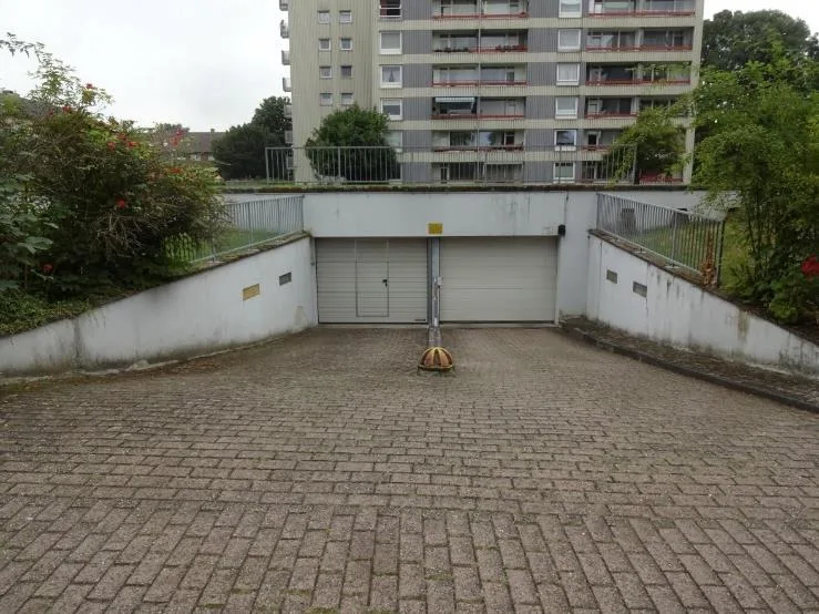 Einfahrt zur Tiefgarage mit Rolltor, dahinter ein mehrgeschossiges Wohnhaus