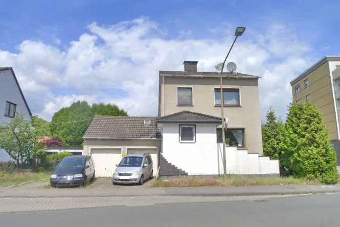 Straßenseitige Außenansicht eines Wohnhauses mit Garage und parkenden Fahrzeugen.