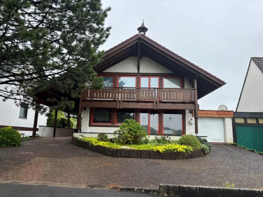 Frontansicht des Wohnhauses mit Balkon, Garage und Vorplatz, unverstellt und gut ausgeleuchtet.