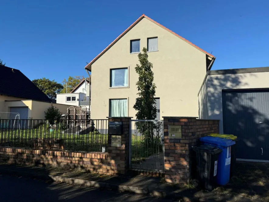 Frontansicht eines Wohnhauses mit Satteldach, Vorgarten, Zaun und Garage, bei Sonne aufgenommen.