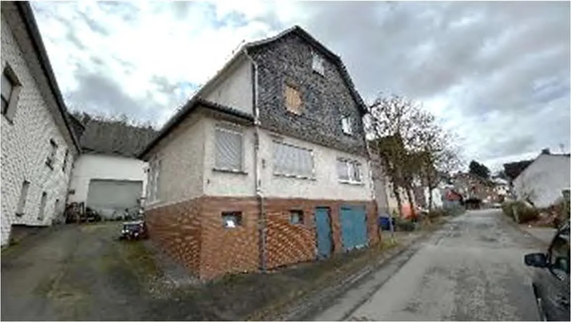 Wohnhaus mit Schieferfassade und Mauerwerkssockel an einer Straße, Außenansicht.
