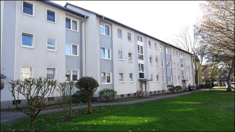 Schräge Außenansicht eines dreigeschossigen Mehrfamilienhauses mit Vorgarten und Rasenfläche.