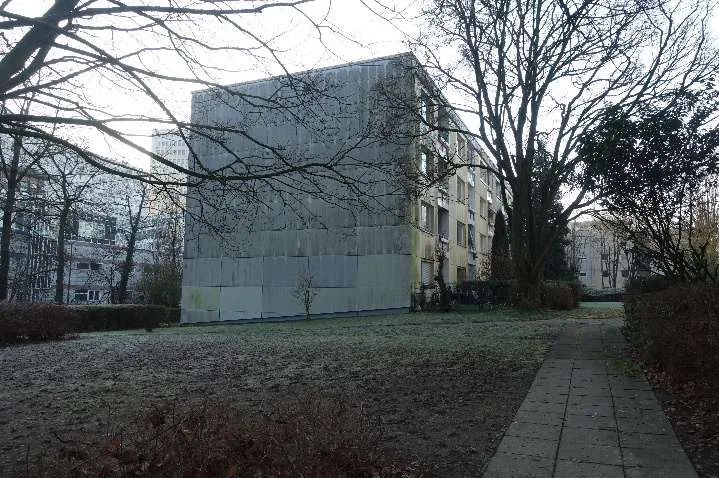 Seitenansicht eines Wohngebäudes mit grauer Fassade über eine Rasenfläche, Weg im Vordergrund.