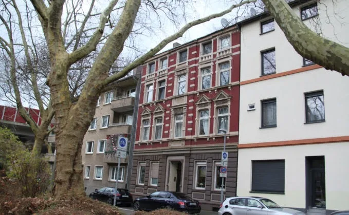 Frontale Außenansicht des Gebäudes mit charakteristischer rot-weißer Fassade und Baum im Vordergrund