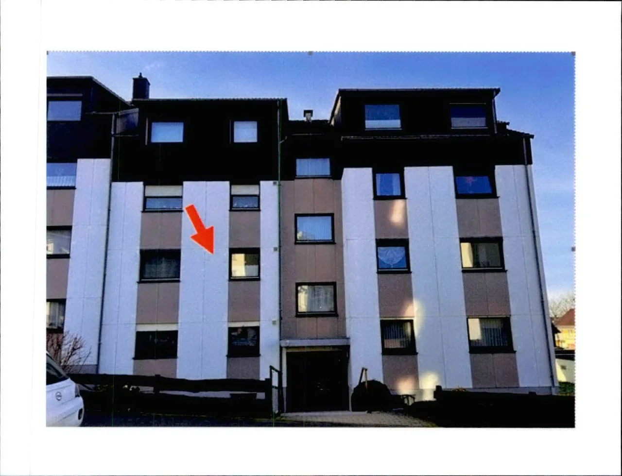 Außenansicht eines mehrgeschossigen Wohnhauses mit roter Pfeilmarkierung auf der Fassade.