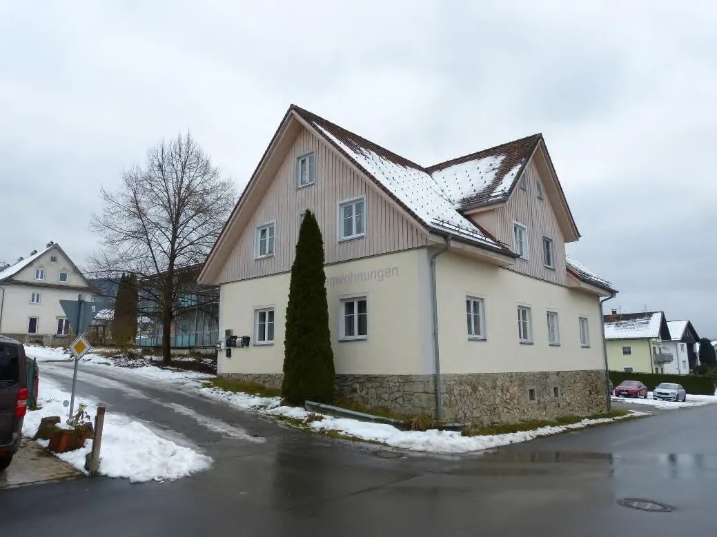 Eckansicht des Wohngebäudes mit heller Putzfassade und Steinsockel, deutlich als Hauptmotiv erkennbar.