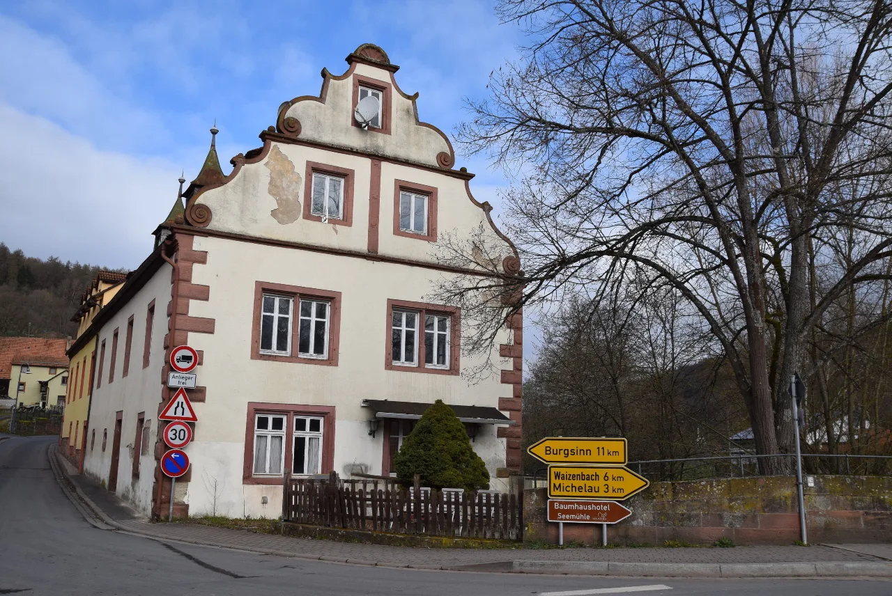 Außenansicht eines zweigeschossigen Giebelhauses an einer Straßenecke, tagsüber bei bewölktem Himmel.