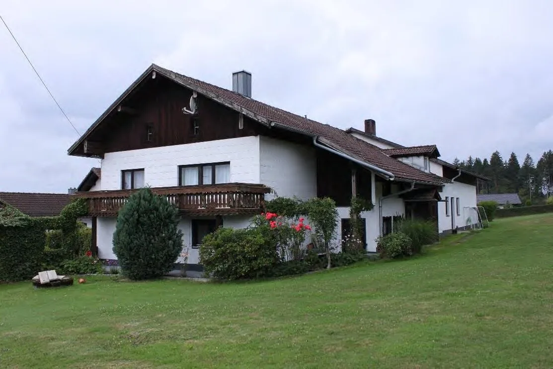 Wohnhaus mit Holzbalkon und dunklem Giebel, Außenansicht von vorne auf Rasenfläche.