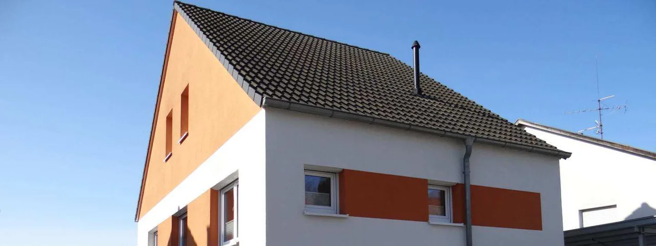 Eckansicht des Einfamilienhauses mit orangefarbener Giebelwand, gut sichtbar vor blauem Himmel