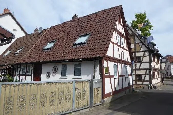 Straßenansicht eines Fachwerkhauses mit Satteldach und Dachfenstern, Zaun im Vordergrund