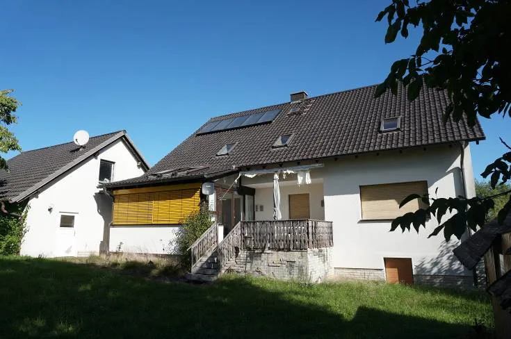 Wohnhaus mit Schrägdach, Solaranlage, Holzterrasse mit Treppe und Rasen im Vordergrund.