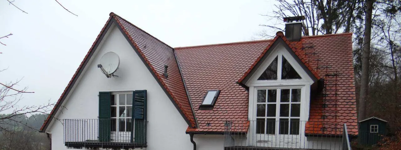 Seitliche Außenansicht des Wohnhauses mit Ziegeldach, Dachgaube, Balkonen und grünem Gartenhäuschen