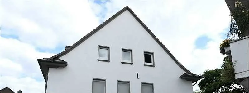 Frontale Ansicht des weiß verputzten Giebelhauses mit Fenstern und Dachgaube