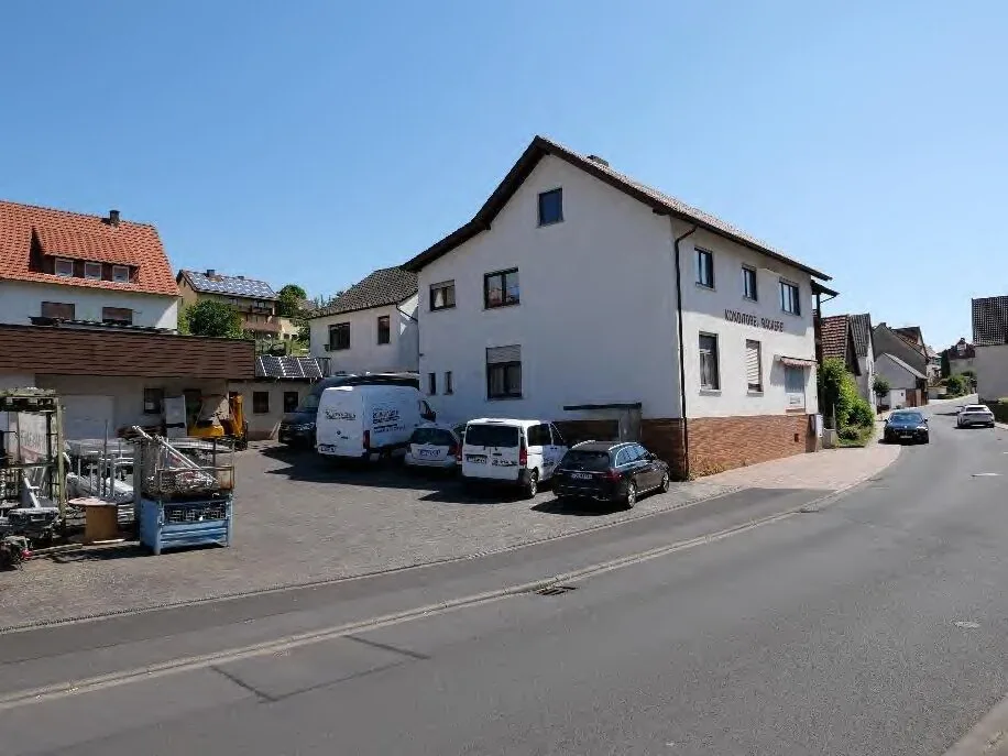 Straßenansicht des Wohn- und Geschäftshauses mit Parkfläche und Fahrzeugen davor
