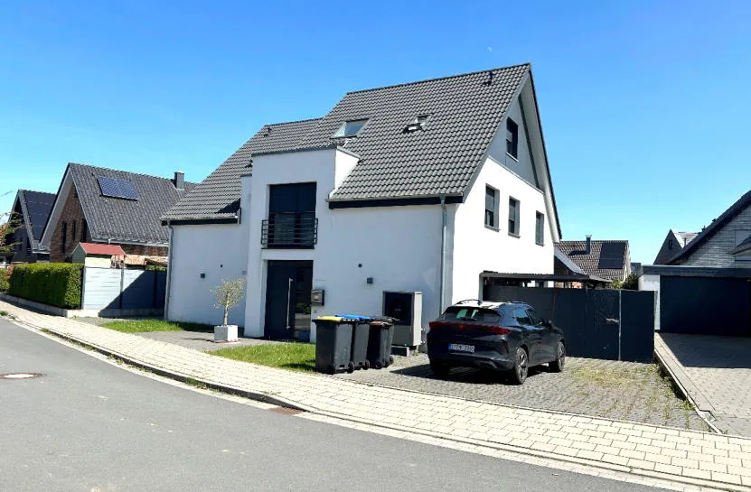 Außenansicht eines weiß verputzten Einfamilienhauses mit Satteldach, Vorfahrt und parkendem Auto