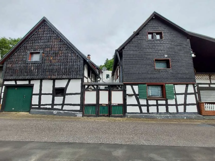 Straßenansicht von zwei Fachwerkhäusern mit dunkler Schieferfassade und grünen Fensterläden