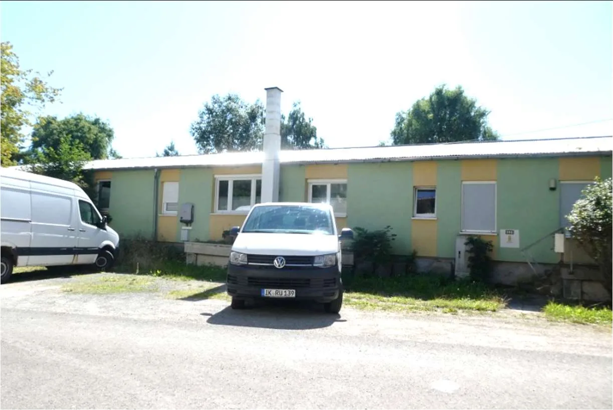 Frontansicht eines langgestreckten, grün-gelb gestrichenen Gebäudes mit Blick auf die Fassade.