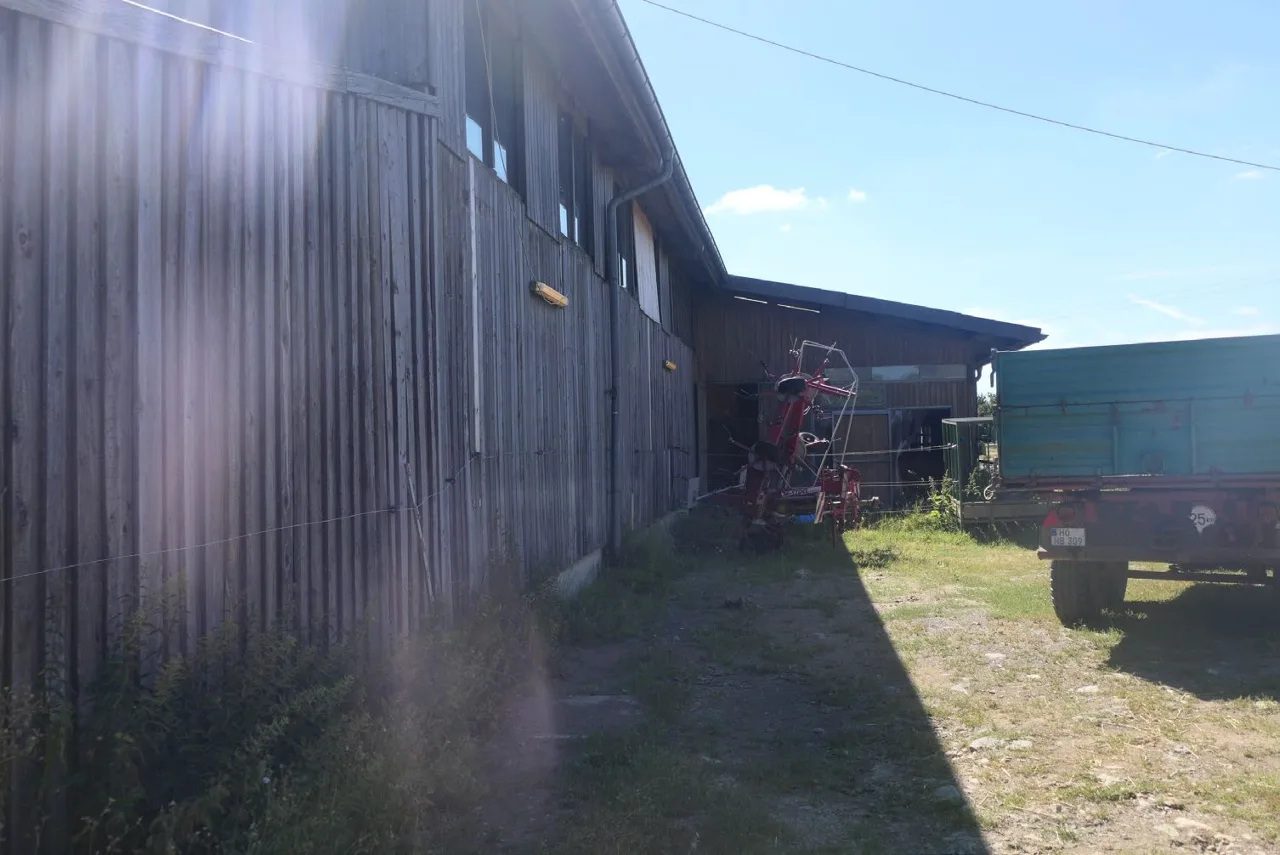 Außenansicht Scheune mit Holzfassade, landwirtschaftliche Geräte und Anhänger davor