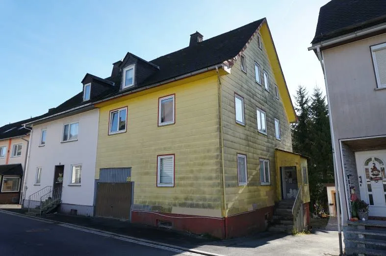 Gelbes Wohnhaus mit Satteldach und Dachgauben, Straßenansicht von schräg vorne, gut sichtbar.