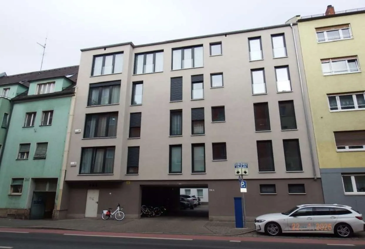 Frontalansicht eines mehrgeschossigen Wohngebäudes mit heller Fassade, Hauseingang und Tiefganeinfahrt, Straßenseite.