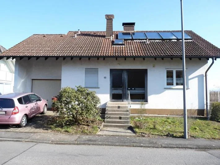 Frontansicht eines Einfamilienhauses mit Garage und parkendem Fahrzeug, gut sichtbar bei Tageslicht.