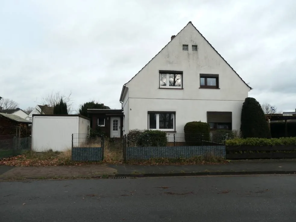 Frontansicht eines freistehenden Einfamilienhauses mit Satteldach, weißer Fassade und Vorgarten; Garage links.