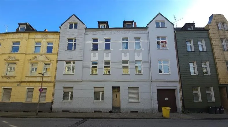 Straßenansicht eines mehrgeschossigen Wohnhauses mit heller Fassade, Eingangstür und Garagentor.