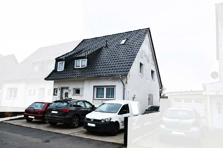 Front view of white house with pitched roof and parking area