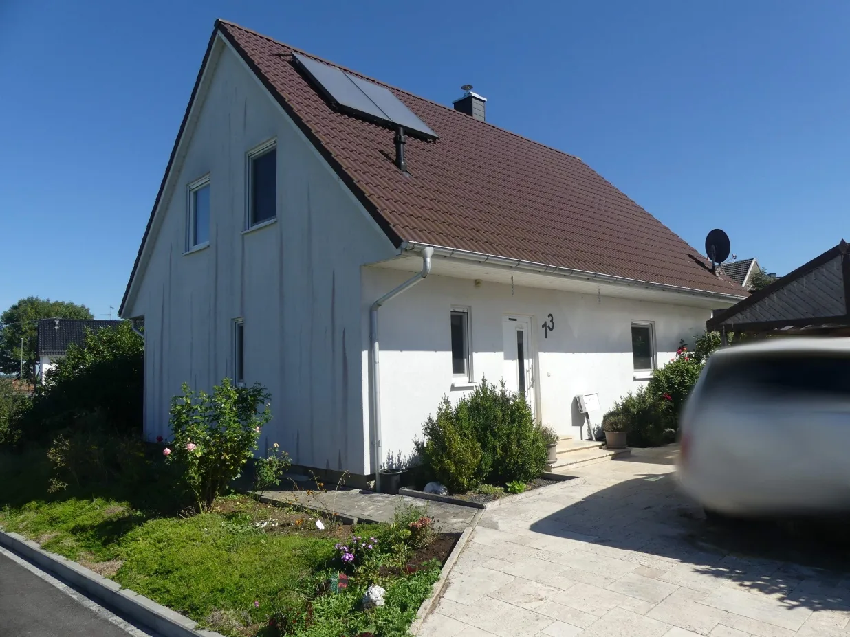 Frontansicht des weiß verputzten Einfamilienhauses mit braunem Satteldach und Hausnummer 13, bei Sonnenschein