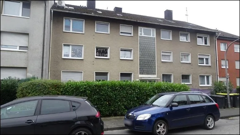 Straßenseitige Frontansicht eines dreigeschossigen Mehrfamilienhauses mit parkenden Fahrzeugen davor