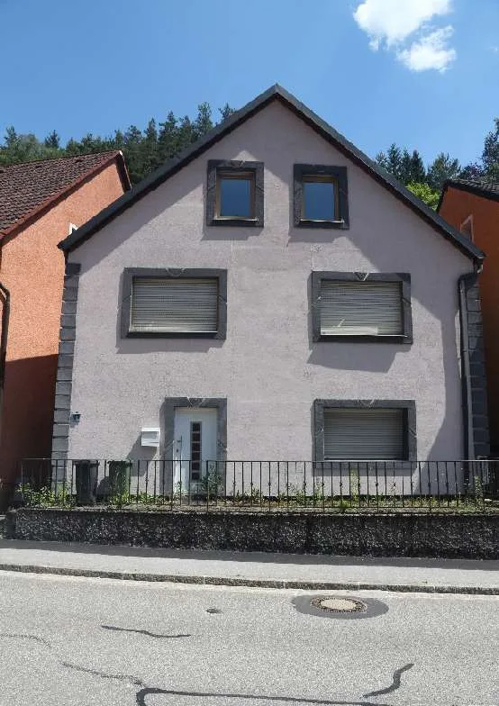 Frontale Außenaufnahme des Wohnhauses mit Satteldach, Fenstern mit Rollläden und Eingangstür.
