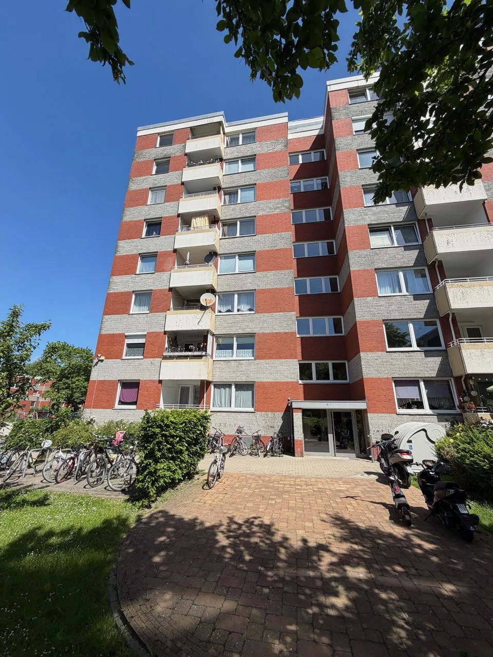 Außenansicht des roten Mehrfamilienhauses mit Balkonen und Fahrradstellplätzen im Vordergrund