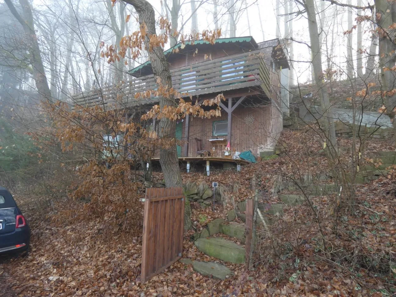 Holzhaus im Wald, Frontansicht mit Balkon und Treppenaufgang, bei Nebel aufgenommen.