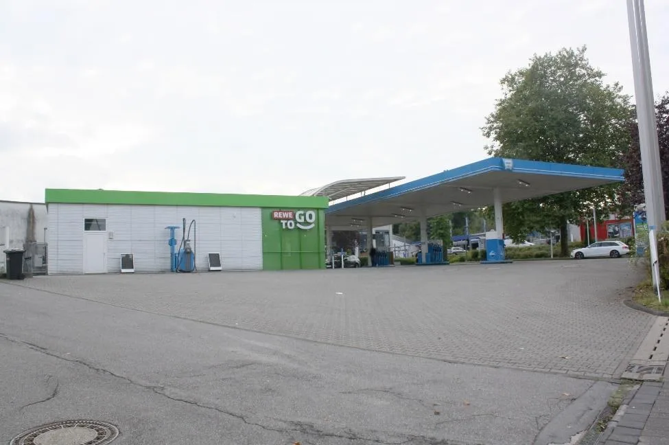 Tankstellengebäude mit grüner Fassade und Überdachung der Zapfsäulen, frontale Ansicht von der Vorfläche.