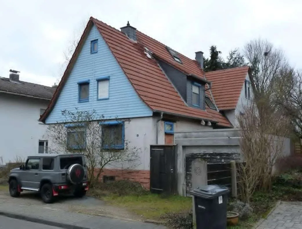 Straßenseite des Wohnhauses mit blauer Holzverkleidung, Ziegeldach und Dachgaube