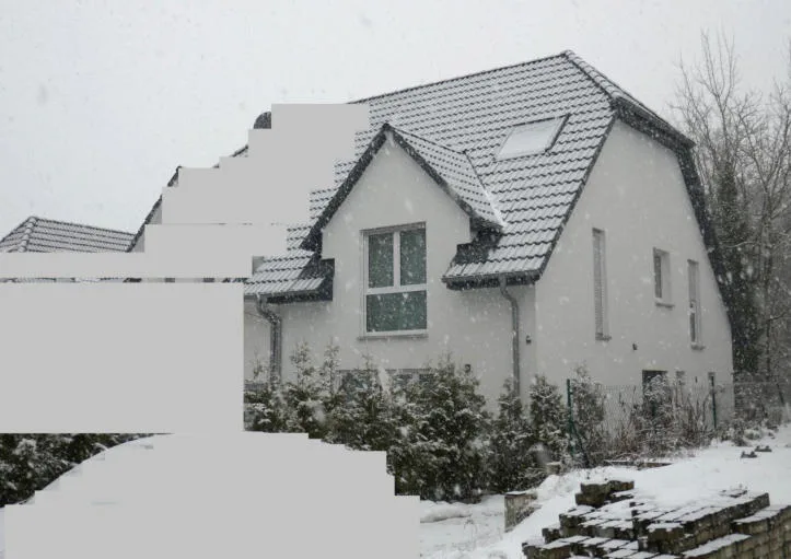 Weißes Einfamilienhaus mit Satteldach und Dachfenster, frontal bis seitlich im Winter fotografiert.