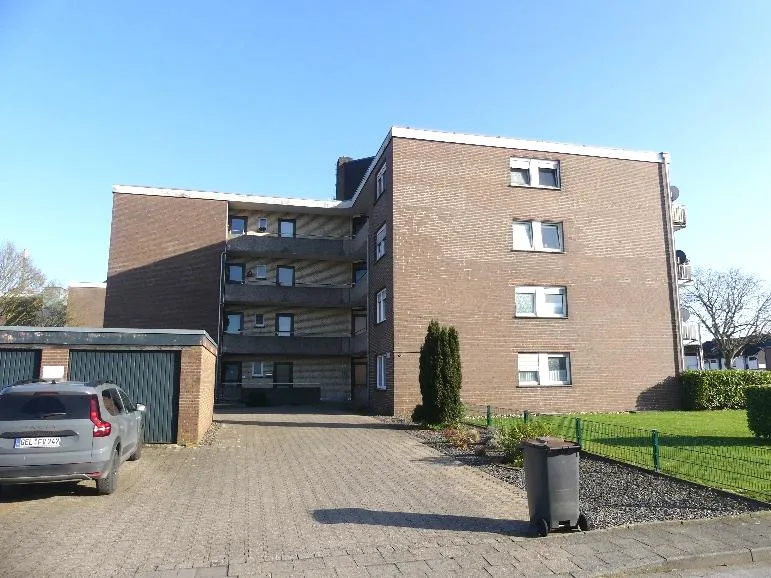 Frontansicht eines mehrstöckigen Wohngebäudes mit Backsteinmauerwerk, moderner Fassade mit Balkonen, Zufahrt und gepflegtem Grundstück