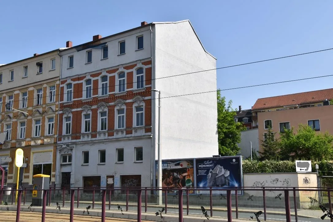Straßenansicht eines mehrgeschossigen Gründerzeit-Wohnhauses mit Klinkerfassade, Brandwand und Werbeplakaten davor, bei Tageslicht.