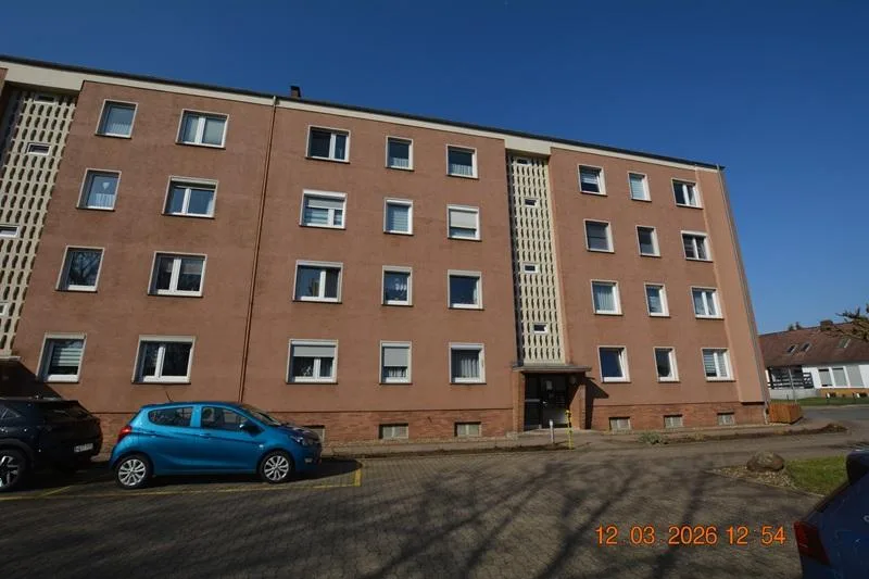 Mehrgeschossiges Wohngebäude mit Klinkerfassade und Balkonen, Frontansicht bei Sonnenschein, Parkplätze davor.