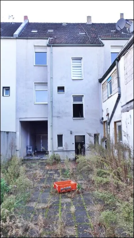 Rückansicht des mehrgeschossigen Wohngebäudes mit Hofbereich, frontal aufgenommen, Dachzone sichtbar.