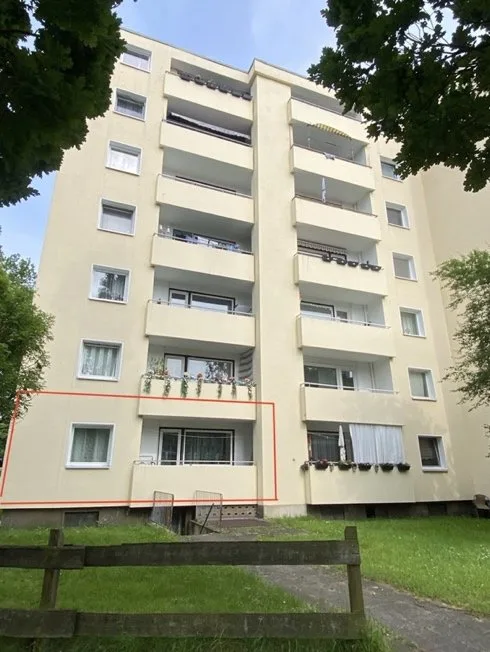 Mehrgeschossiges Wohngebäude von vorne, Balkone sichtbar; Wohneinheit farbig umrandet markiert.