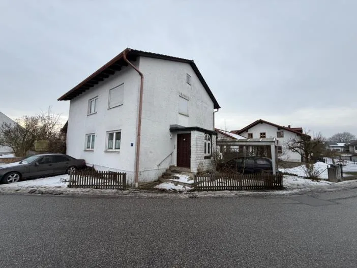 Frontalansicht eines weißen Wohnhauses mit Satteldach und zwei Fensterreihen, parkender Pkw davor.