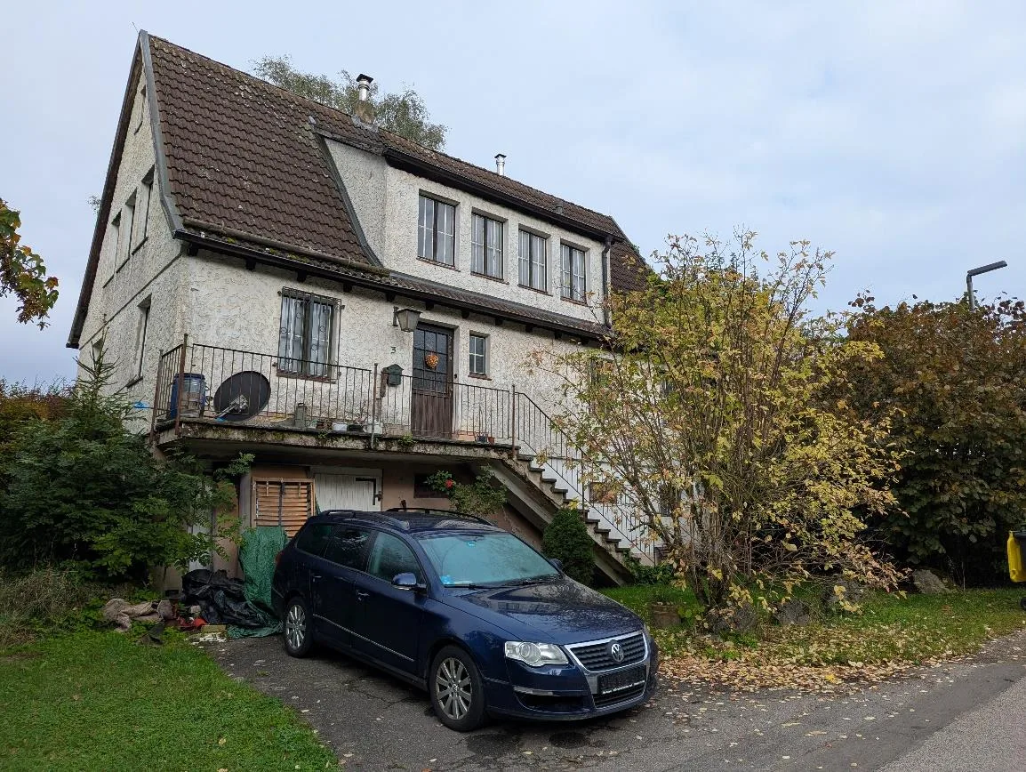 Frontansicht des Wohnhauses mit Satteldach, Balkon und davor geparktem blauen Kombi