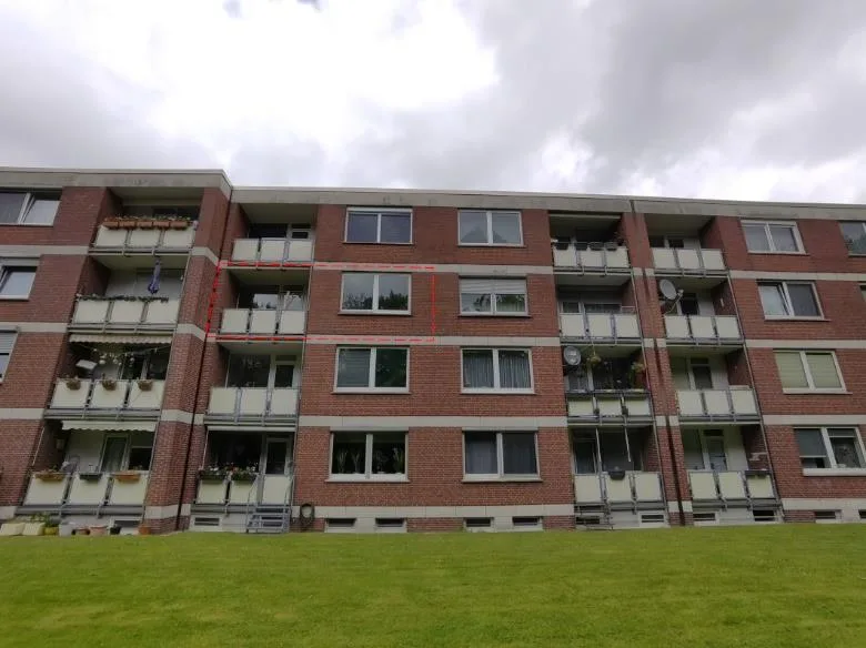 Mehrgeschossiges Wohnhaus mit Balkonen von vorne, eine Wohneinheit rot umrandet markiert.