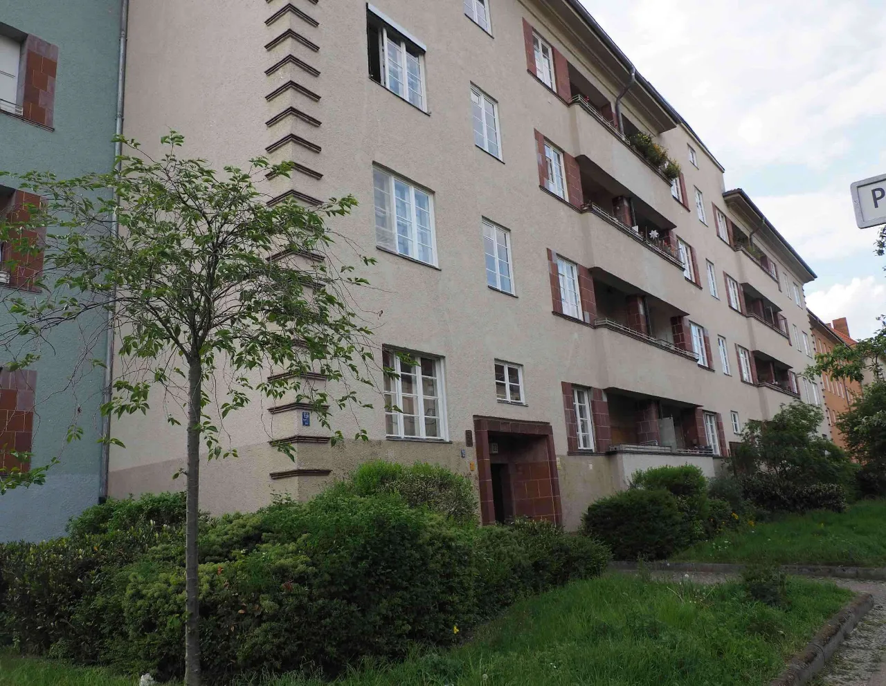 Straßenansicht des Mehrfamilienhauses mit Balkonen, schräg aufgenommen und teilweise von einem Baum verdeckt
