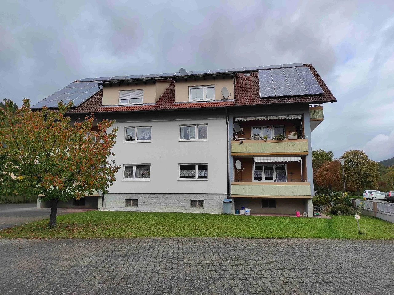 Mehrfamilienhaus mit Balkonen und Photovoltaikdach, frontale Außenansicht über eine Rasenfläche.